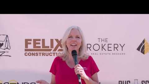 woman with grey hair wearing a pink shirt stands with a microphone